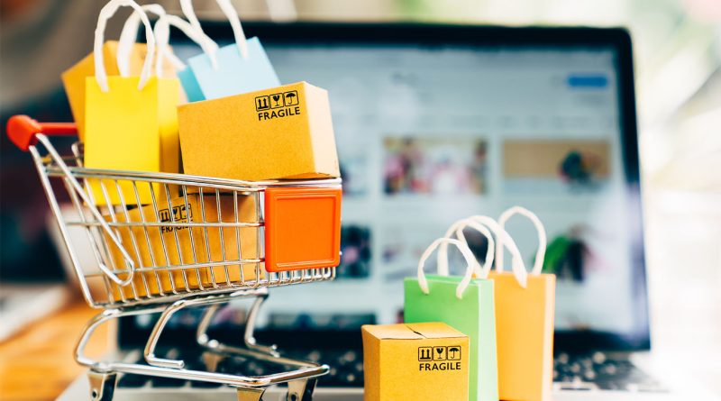 Image of a small shopping cart filled with various bags in front of a laptop to support online shopping article
