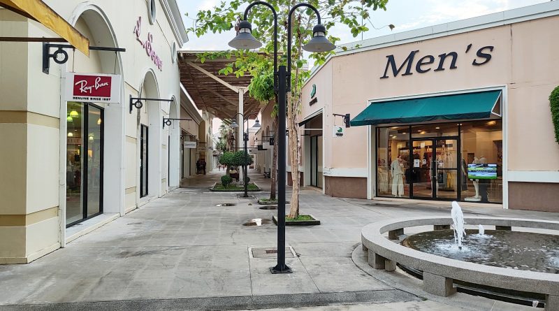 Image of a premium outlet centre with various different shop fronts on display and a large palm tree in the middle