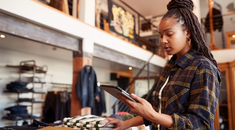 Image of a woman in a shop with a scanner and different clothing products to support US retail sales article