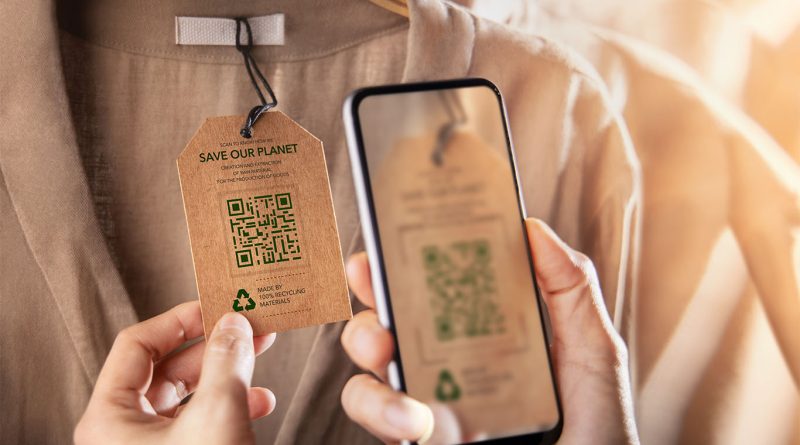 Close-up of a person scanning a sustainable clothing tag with a smartphone, showing a QR code and recycling message on a garment made from 100% recycled materials.