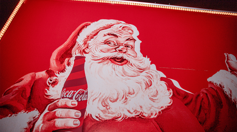Vintage Coca-Cola Christmas advertisement featuring Santa Claus holding a classic Coke bottle on a bright red background