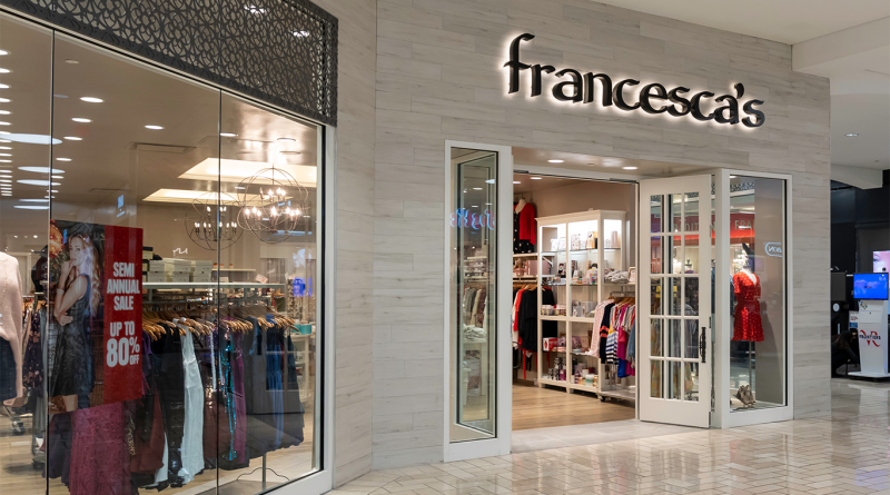 Exterior of a Francesca’s boutique store in a shopping mall with glass windows, promotional signage for a semi-annual sale, and racks of clothing visible inside.