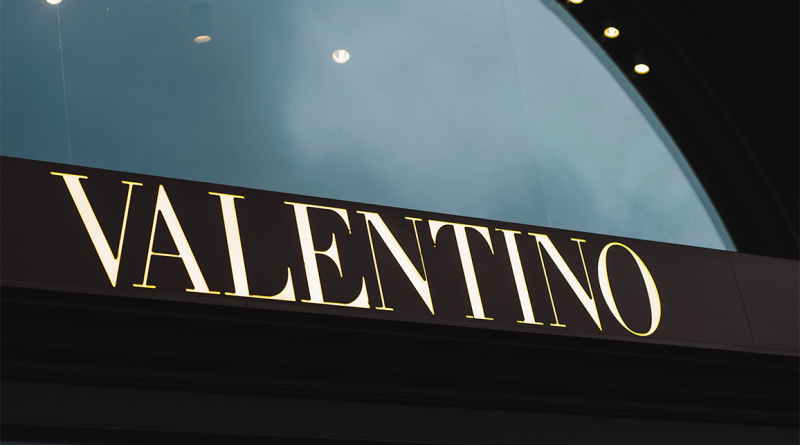 Illuminated Valentino store sign against a reflective glass background, representing the global fashion house’s luxury presence