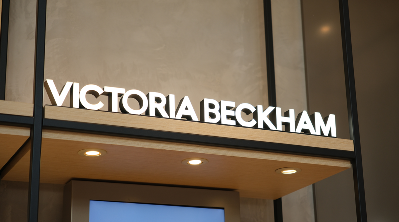 Illuminated “VICTORIA BECKHAM” sign above a sleek retail entrance, suggesting a luxury fashion or beauty store setting.