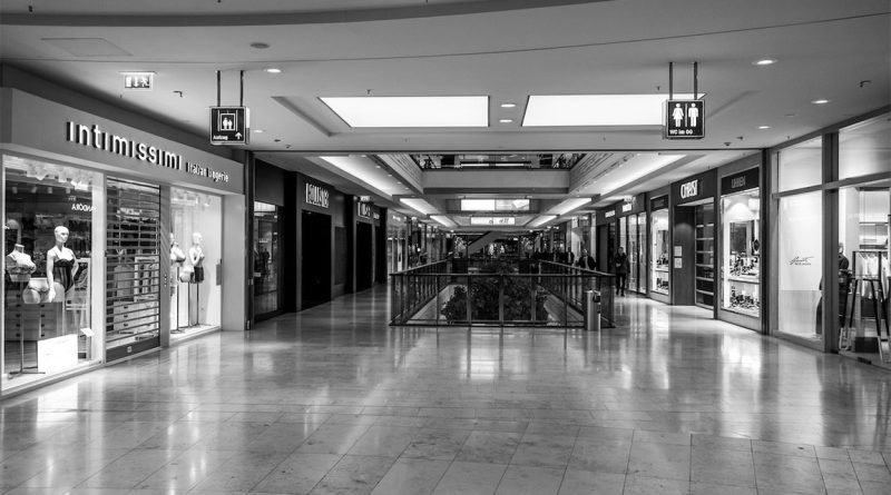nterior view of a modern shopping mall corridor with retail storefronts, tiled flooring and overhead signage.